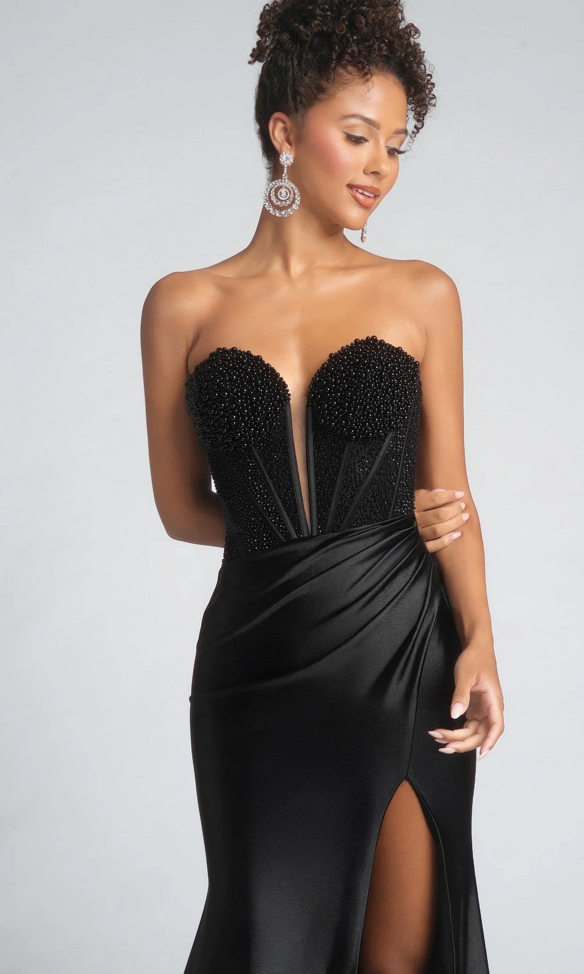 A woman in the Portia and Scarlett PS26039 long prom dress with a beaded corset bodice, thigh-high slit, and statement earrings poses against a neutral background.